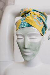 white mannequin bust wearing a green beauty spa clay face mask with head wrap towel