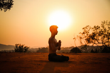 Young man doing yoga exercise meditation at the sunset on a top of the mountain with sun behind