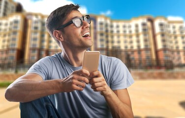 Happy smiling young man looking at smatrphone in his hand with excited face expression,