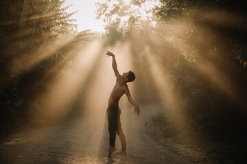 Young man doing yoga dance in the nature with a beautiful fog light in the middle of the light rays 