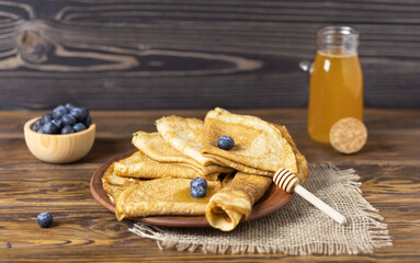 Pancakes are thin homemade pancakes with berries, with a bottle of honey on a wooden table. Traditional Russian cuisine. Selective focus.