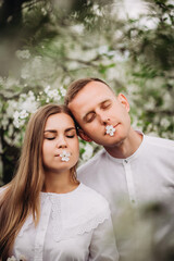 Fototapeta premium Young loving couple in a walk in a spring blooming apple orchard. Happy married couple enjoy each other while walking in the garden. Man holding woman's hand
