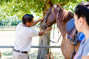 male riding instructor, teaching his student how to put on the bridle and the mouth-lock.