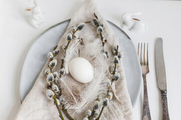 Stylish Easter table setting. Natural easter egg, pussy willow branches, feathers on modern plate...