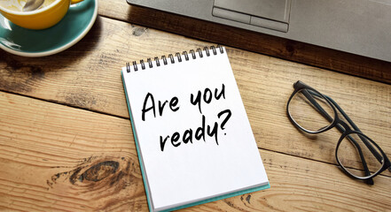 Notepad with the inscription ARE YOU READY, laptop, glasses and a cup of coffee on the table. Conceptual image. Finance or business concept.