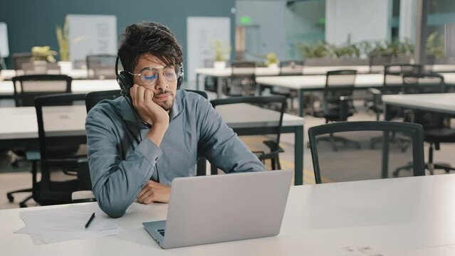 Bored man Arabian man Indian service manager in headphones have displeased look video conference webinar learn language improve self-education professional skills studying with difficult task boredom