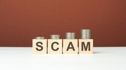 scam text on wooden blocks with coins on brown background