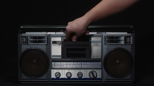 A man's hand inserts a cassette into an old vintage cassette recorder and presses the play button