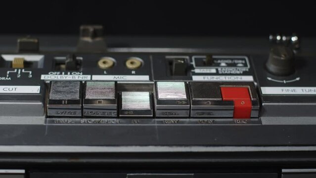 A finger presses the rewind button on an old shiny cassette recorder - close-up