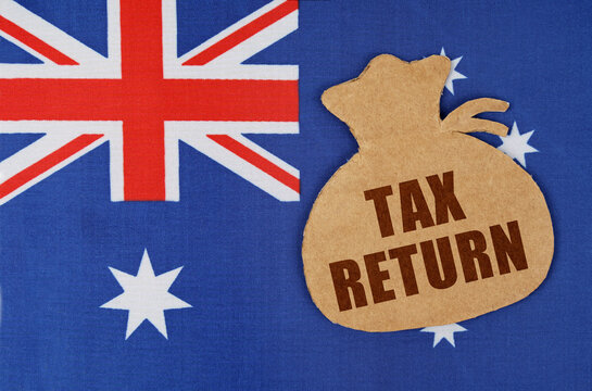 On The Flag Of Australia Lies A Cardboard Figure Of A Money Bag With The Inscription - TAX RETURN