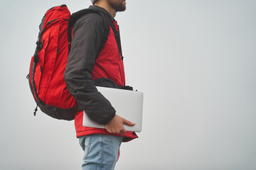 Digital nomad with laptop and backpack travelling while working on scandinavian location with mist