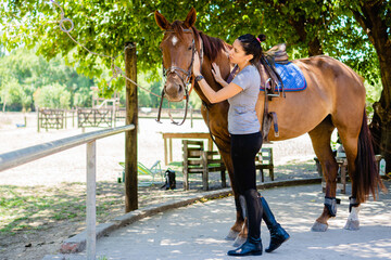 young latina woman rider caressing her horse in the field