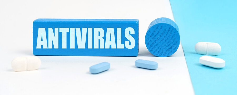 On a white and blue surface are pills, a pen and a wooden sign with the inscription - Antivirals