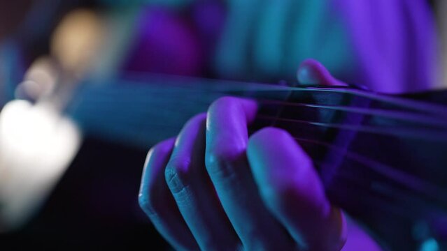 Hand of woman touching strings of guitar performing on stage illuminated by dark purple light. Musician enjoys playing musical instrument extreme closeup