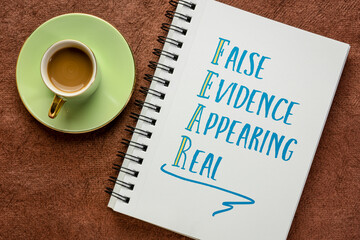 FEAR acronym - false evidence appearing real, handwriting in a sketchbook with a cup of coffee, business concept