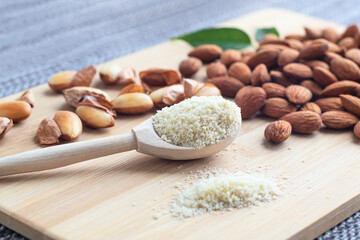 Close-up of almond flour in a wooden spoon, almond kernels, peeled and not, on a wooden board on a napkin.