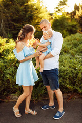 Naklejka premium Little cute baby girl with mom and dad, beautiful daughter sitting on strong fathers arms and smile to caring mother, happy young family at the park