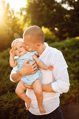 Handsome man with adorable baby girl at the park, smiling, caring father kiss little daughter, loving dad and cute toddler spend time together, parenthood concept