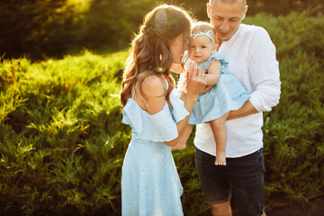 Obraz premium Little cute baby girl with mom and dad, beautiful daughter sitting on strong fathers arms and smile to caring mother, happy young family at the park