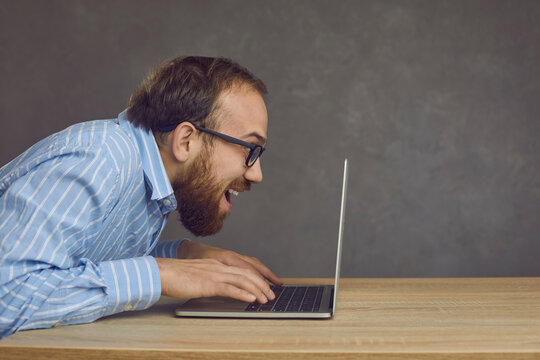 Funny caucasian man typing fast on laptop keyboard, male gamer playing video game, crazy looking computer geek studio shot. Online work, technology, internet and communication concept