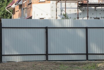 part of a gray metal fence wall with a black iron frame on a rural street