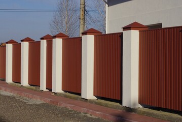 long red metal fence wall with white concrete columns on a rural street