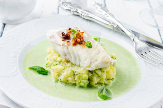 Traditional skrei cod fish filet mashed potatoes in basil champagne foam served as close-up on a classic plate