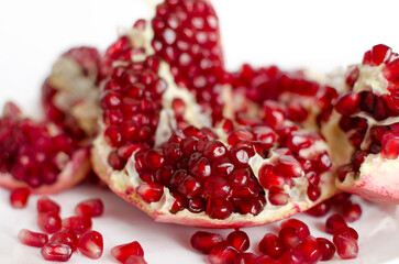 Red ripe pomegranate cut seeds are fresh close-up on a white plate. Juicy fruit, vitamins