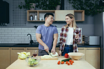 Happy young family, man and woman, cooking together, Asian cuts vegetables, date at home, romantic evening