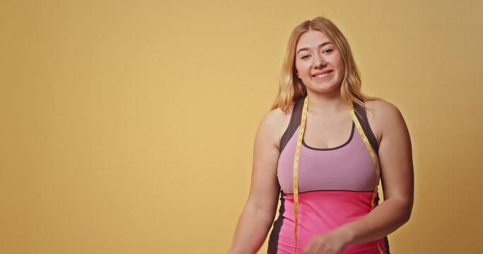 Young smiling happy fun chubby overweight plus size big fat fit woman in red top hold measuring tape point finger on waist warm up train isolated on purple background home gym. Workout sport concept