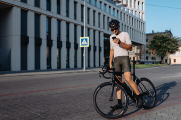 Obraz na płótnie Canvas Cyclist standing on street with bike and using smartphone