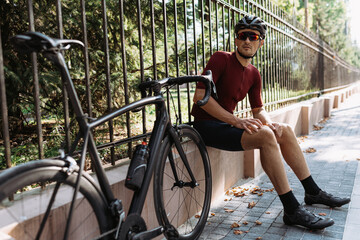 Tired cyclist sitting near metal fence with sport bike