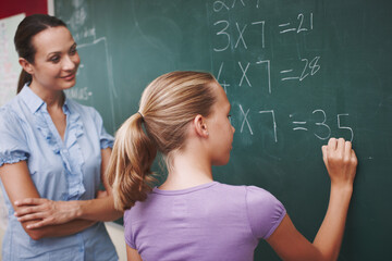 Improving on her mathematics. A pretty young teacher helping her student with a maths problem at...