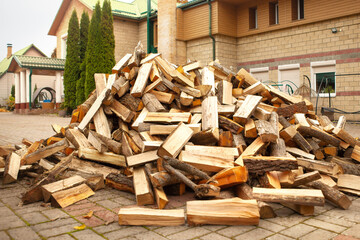A pile of split firewood for heating the house, unloaded in the yard, against the backdrop of the house, natural heating sources.