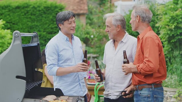 Three senior male friends cooking outdoor barbeque and drinking beer at home together - shot in slow motion