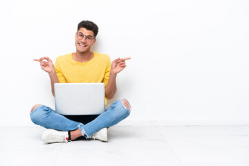 Young man sitting on the floor isolated on white background pointing finger to the laterals and...