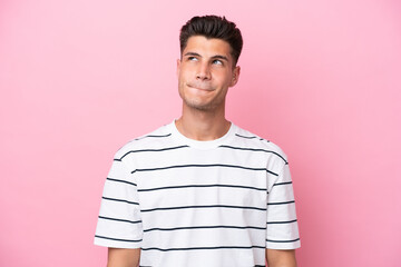 Young caucasian man isolated on pink background having doubts while looking up