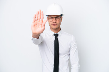 Young architect caucasian man with helmet and holding blueprints isolated on white background making stop gesture