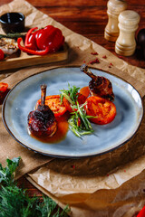Fried quail legs with tomatoes on a plate, top view