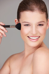 Fototapeta premium Just a light blush.... Studio shot of a beautiful woman applying blush to her cheeks.