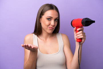 Young caucasian woman holding a hairdryer isolated on purple background making doubts gesture while lifting the shoulders