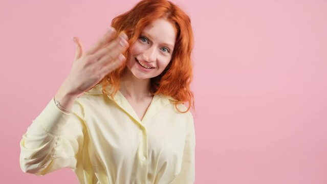 Beautifal young pretty woman with red hair smiling and making knock sign for calling somesody to come and pointing with her hand aside.