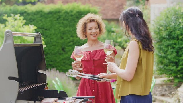Two mature female friends cooking outdoor barbeque and drinking wine at home - shot in slow motion