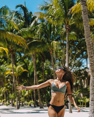 Modelo femenina posando en bikini en una playa paradisíca con palmeras