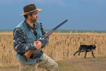 Hunter man in camouflage with a gun during the hunt in search of wild birds or game. Autumn hunting...