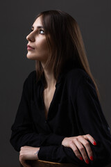 Fototapeta premium Portrait of a young brunette with long hair in the studio. Dramatic photo in dark colors.