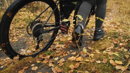 The woman travel on mixed terrain cycle touring with bikepacking. The traveler journey with bicycle bags. Sportswear in green black colors. The trip in magical autumn forest. Wooden bridge, river.