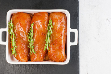 Marinated chicken fillet in red sauce in a roasting plate on a dark background. Raw marinated chicken fillet with fresh rosemary. Convenience food.