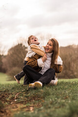 Happy mother with daughter sitting in  park on a grass.Both laughing and have a fun.