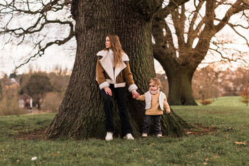 Mother and daughter stand in the midst of trees, with arms outstretched. Looking to one way.